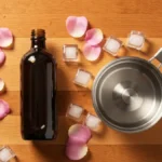 Domowy hydrolat różany w szklanej butelce z płatkami róży obok garnka na drewnianym blacie kuchennym