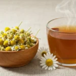 Suszone kwiaty rumianku pospolitego w drewnianej miseczce obok filiżanki herbaty rumiankowej na naturalnym tle lnianej tkaniny