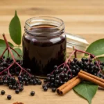 Domowy syrop z czarnego bzu w szklanym sloiku otoczony swiezymi owocami bzu i lisciami na drewnianym stole
